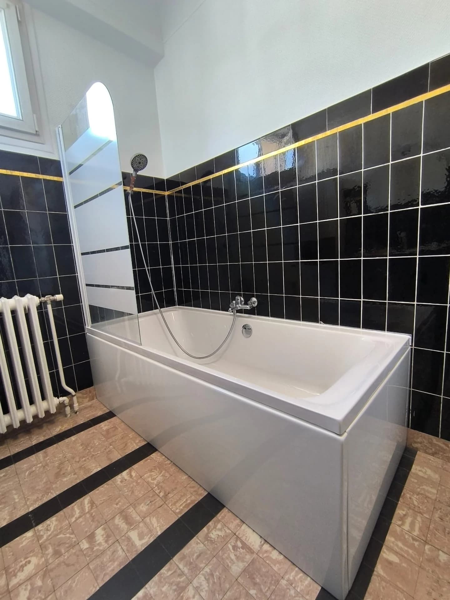 Baignoire blanche dans une salle de bain aux murs carrelés noirs