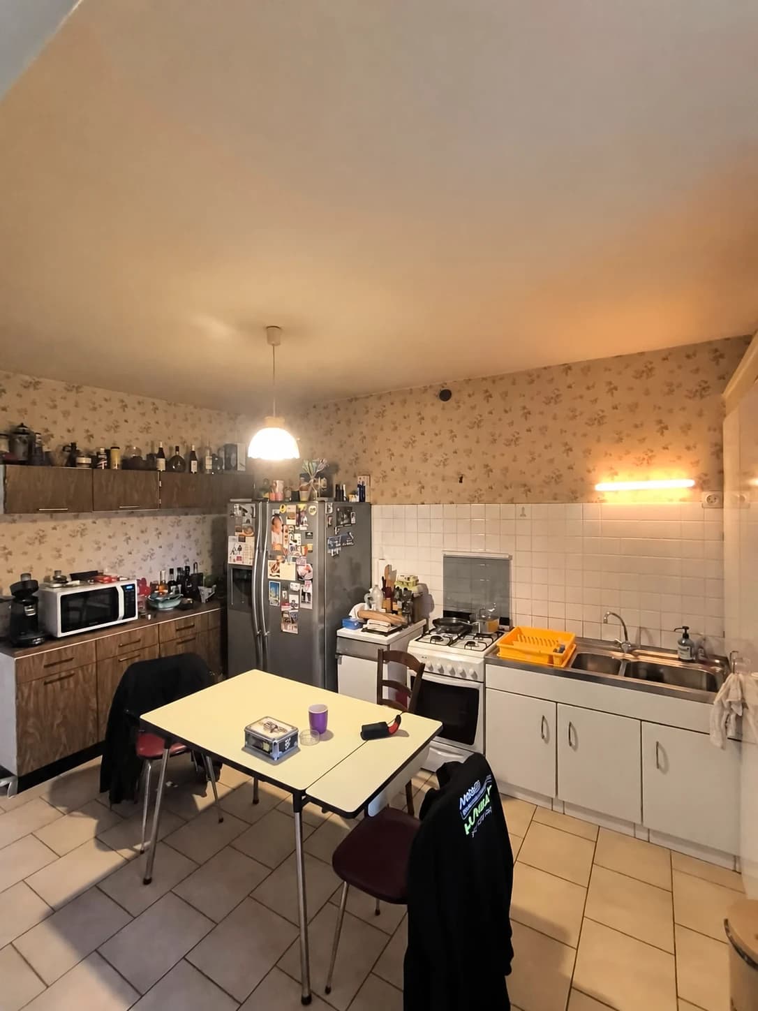 Cuisine avant travaux avec meubles anciens, papier peint et table centrale